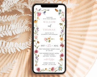 May include: A floral wedding invitation on a smartphone screen. The invitation features a wreath of watercolor flowers and the text "Together with their families Willow and Thomas invite you to celebrate their wedding. Sat 25 Aug Two Thousand Twenty XXXX at 3:00 PM The Summer Valley Hotel 123 Smith Street Anytown CA 45678 reception to follow Kindly RSVP to Willow 123 456 7890"