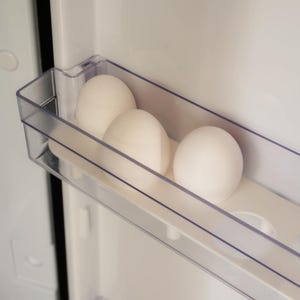 Könnte beinhalten: Drei weiße Eier liegen in einem transparenten Eierhalter im Kühlschrank. Die Eier sind oval und sehen frisch aus. Der Kühlschrankinnenraum ist weiß und hat ein schlichtes, sauberes Design.