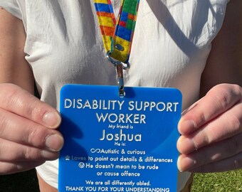 May include: Blue plastic badge with the text "Disability Support Worker" and "My friend is Joshua" with a description of Joshua's personality traits. The badge is being held by a person.