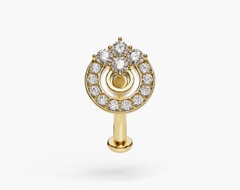 Op de afbeelding: Een gouden neusring met een cirkelvormig ontwerp met een cluster van kleine diamanten in het midden en een grotere cirkel van diamanten rond de rand.