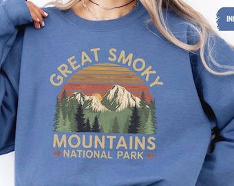 Könnte beinhalten: Ein blaues Sweatshirt mit einem Vintage-Grafikdesign mit dem Text "Great Smoky Mountains National Park" und einer Sonnenuntergangsszene mit Bergen und Bäumen.