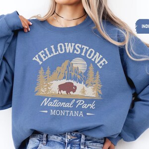 May include: A blue sweatshirt with the text "Yellowstone National Park - Montana" and a graphic of a bison in a forest setting.