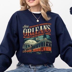 May include: Navy blue sweatshirt with a vintage-style graphic of a streetcar in New Orleans. The text "New Orleans" is in a retro font.