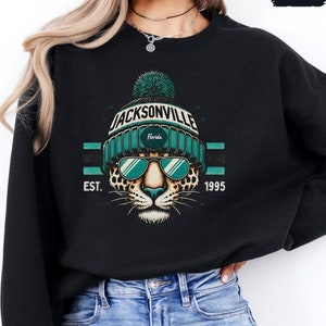May include: Black sweatshirt with a graphic of a leopard wearing a teal beanie with the text "JACKSONVILLE Florida EST. 1995".