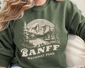 May include: A green sweatshirt with a graphic of a mountain range and a lake with the text "Banff National Park" in a retro font.