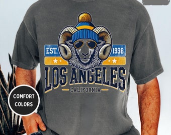Op de afbeelding: Een grijs T-shirt met een vintage-stijl grafische afbeelding van een ram die een blauwe en gele muts en een zonnebril draagt. De afbeelding zegt "EST. 1936 LOS ANGELES CALIFORNIË".