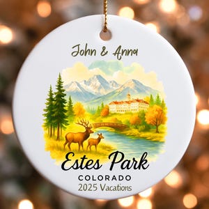May include: White ceramic ornament with a scenic illustration of Estes Park, Colorado. The design includes mountains, a river, trees, and two deer. Text reads "John & Anna", "Estes Park, Colorado, 2025 Vacations". A gold string is attached for hanging.