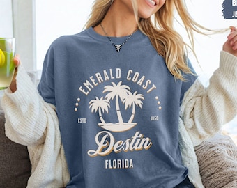 May include: A blue jean t-shirt with a white graphic design that says "Emerald Coast" with palm trees and "Destin, Florida" in a vintage style font.