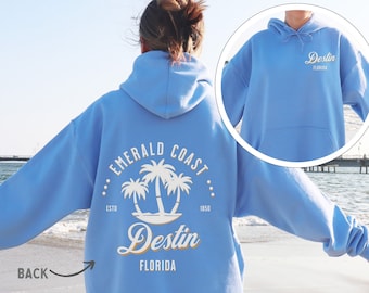May include: A light blue hoodie with a white graphic on the back that says "Emerald Coast Destin Florida" with palm trees. The front of the hoodie has a white graphic that says "Destin Florida".