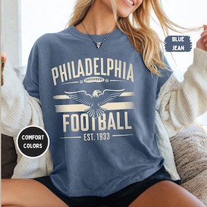 May include: A blue jean t-shirt with a white graphic of an eagle and the text "Philadelphia Football Est. 1933".