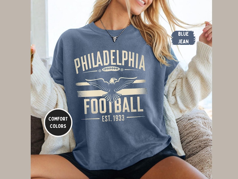 May include: A blue jean t-shirt with a white graphic of an eagle and the text "Philadelphia Football Est. 1933".
