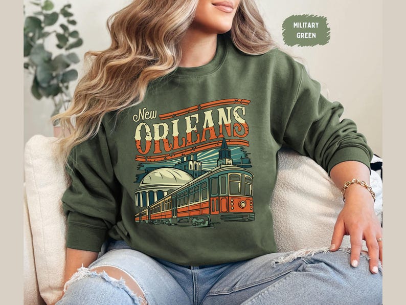May include: A green sweatshirt with a vintage-style graphic of a streetcar in New Orleans. The text "New Orleans" is printed in a bold, retro font.