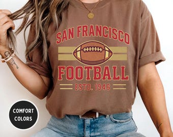 May include: Espresso-coloured t-shirt with a San Francisco Football graphic. The design features the text "SAN FRANCISCO FOOTBALL" above a football graphic, with "ESTD. 1946" below. The shirt is a comfort colour.
