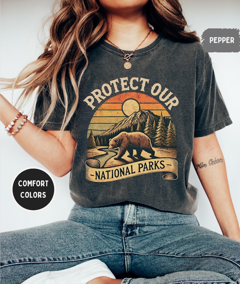 May include: A dark gray t-shirt with a vintage-style graphic of a bear in a forest with the text "Protect Our National Parks".