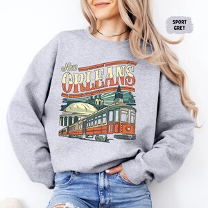 May include: A gray sweatshirt with a vintage-style graphic of a streetcar in New Orleans. The text "New Orleans" is in a bold, colorful font.