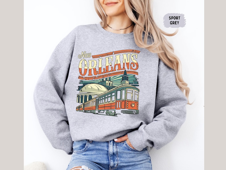 May include: A gray sweatshirt with a vintage-style graphic of a streetcar in New Orleans. The text "New Orleans" is in a bold, colorful font.