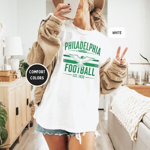 May include: White t-shirt with green and white graphic print that says "Philadelphia Football Est. 1933" with a stylized eagle design.