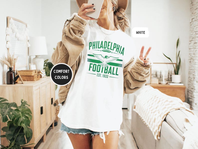 May include: White t-shirt with green and white graphic print that says "Philadelphia Football Est. 1933" with a stylized eagle design.
