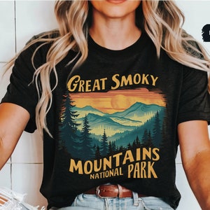 May include: A black t-shirt with a vintage-style graphic of the Great Smoky Mountains National Park. The graphic features a sunset over the mountains with a yellow sun and a blue sky. The text "Great Smoky Mountains National Park" is in yellow and white.