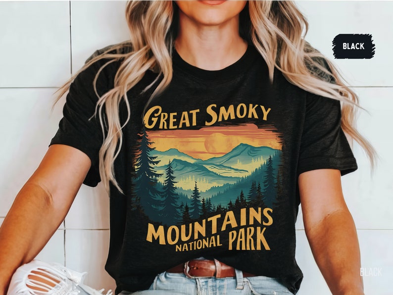May include: A black t-shirt with a vintage-style graphic of the Great Smoky Mountains National Park. The graphic features a sunset over the mountains with a yellow sun and a blue sky. The text "Great Smoky Mountains National Park" is in yellow and white.