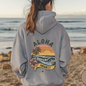 Puede incluir: Sudadera con capucha gris con un gr&aacute;fico de estilo retro en la espalda que dice "Aloha Hawaii" con un dise&ntilde;o de palmera, puesta de sol y ola.