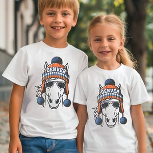 Könnte beinhalten: Zwei Kinder tragen weiße T-Shirts mit einem Pferde-Motiv. Das Pferd trägt einen Hut mit dem Wort "DENVER" und eine Sonnenbrille. Der Hut ist orange, blau und weiß. Das Pferde-Motiv ist mittig auf den Shirts platziert.