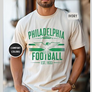 May include: A white t-shirt with a green and white graphic design that says "Philadelphia Football Est. 1933". The graphic features a stylized eagle with wings spread.