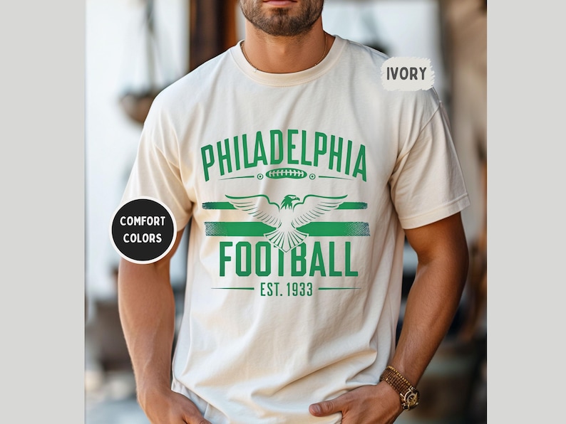 May include: A white t-shirt with a green and white graphic design that says "Philadelphia Football Est. 1933". The graphic features a stylized eagle with wings spread.