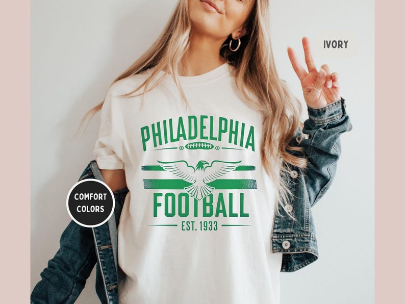 May include: White t-shirt with green text that reads "Philadelphia Football Est. 1933". The text is surrounded by a green and white stripe design. A green eagle with outstretched wings is centered above the text.
