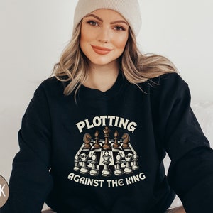 May include: Black sweatshirt with a chessboard graphic and the text "Plotting Against The King".
