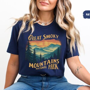 May include: A navy blue t-shirt with a vintage-style graphic of a mountain range and sunset. The text "Great Smoky Mountains National Park" is printed on the shirt.