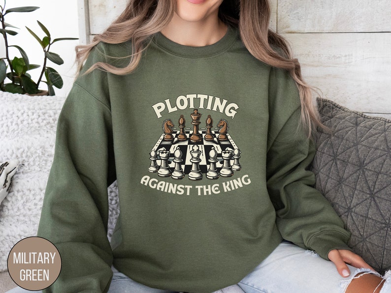 May include: A green sweatshirt with the text "Plotting Against The King" and a graphic of a chessboard with chess pieces.