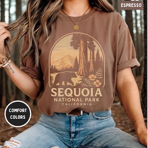 Puede incluir: Camiseta marrón con un diseño del Parque Nacional de las Secuoyas. El diseño incluye un oso, árboles, montañas y el texto "SEQUOIA NATIONAL PARK CALIFORNIA". La camiseta es de color "ESPRESSO" y tiene la etiqueta "COMFORT COLORS".