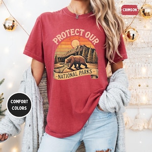May include: A red t-shirt with a vintage-style graphic of a bear in a forest with the text "Protect Our National Parks".