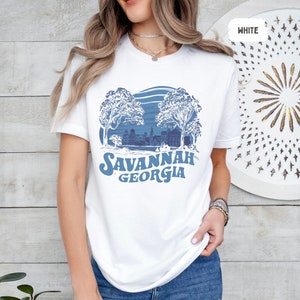 Puede incluir: Camiseta blanca con un dise&ntilde;o gr&aacute;fico azul de una ciudad con &aacute;rboles y el texto "SAVANNAH GEORGIA".