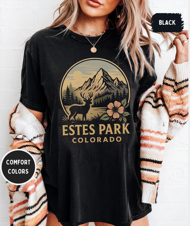 May include: Black t-shirt with a circular graphic featuring a mountain range, a deer, and a flower. The text "ESTES PARK COLORADO" is below the graphic. The shirt also has the text "COMFORT COLORS" on a circular sticker.