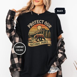May include: Black t-shirt with a vintage-style graphic of a bear in front of a mountain and sunset. The text "Protect Our National Parks" is printed on the shirt.