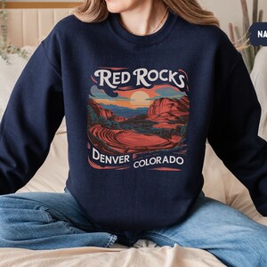 May include: A navy blue sweatshirt with a graphic print of a sunset over red rocks. The text "Red Rocks Denver Colorado" is printed below the graphic.