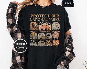 May include: Black t-shirt with the text "Protect Our National Parks" and illustrations of different national parks, including Yosemite, Yellowstone, Joshua Tree, Acadia, Olympic, Glacier, Zion, Mount Rainier, Grand Teton, Shenandoah, and Arches.