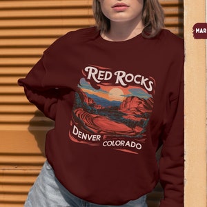 May include: A maroon sweatshirt with a graphic print of a red rock landscape. The text "Red Rocks Denver Colorado" is printed on the sweatshirt.