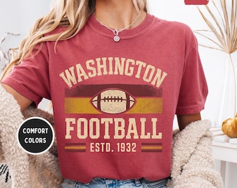 Op de afbeelding: Een bordeauxrood t-shirt met de woorden "WASHINGTON FOOTBALL" in een vintage lettertype, met een football-afbeelding. Het shirt bevat ook "ESTD. 1932" en de woorden "COMFORT COLORS" in een cirkel.