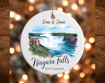 May include: White ceramic ornament with a watercolor illustration of Niagara Falls. The ornament features the text "Dan & Jane" and "Niagara Falls 2024 Engagement".