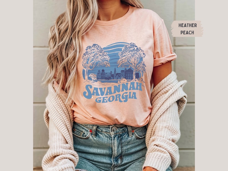 Puede incluir: Una camiseta de color melocot&oacute;n jaspeado con un gr&aacute;fico azul de una ciudad con &aacute;rboles y el texto "Savannah Georgia".