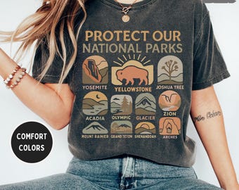May include: A dark grey t-shirt with the text "Protect Our National Parks" and illustrations of different national parks, including Yosemite, Yellowstone, Joshua Tree, Acadia, Olympic, Glacier, Zion, Mount Rainier, Grand Teton, Shenandoah, and Arches.