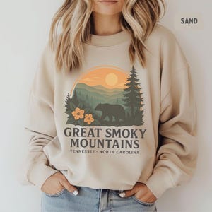 Könnte beinhalten: Sandfarbenes Sweatshirt mit einem Grafikdesign der Great Smoky Mountains. Das Design zeigt eine Bärensilhouette, Bäume, Berge und den Text "Great Smoky Mountains Tennessee North Carolina."
