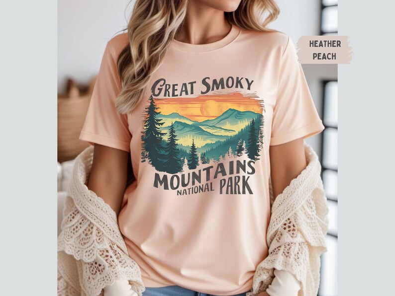 May include: A heather peach t-shirt with a vintage-style graphic of a mountain range with a sunset and the text "Great Smoky Mountains National Park".