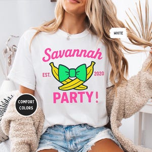 May include: White t-shirt with the text "Savannah PARTY!" in pink, with a green bow and yellow bananas graphic. The text "EST. 2020" is also included. The shirt is labeled "COMFORT COLORS" and "WHITE".