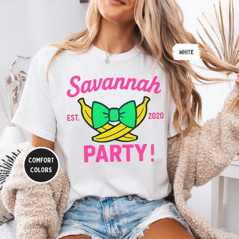 May include: White t-shirt with the text "Savannah PARTY!" in pink, with a green bow and yellow bananas graphic. The text "EST. 2020" is also included. The shirt is labeled "COMFORT COLORS" and "WHITE".