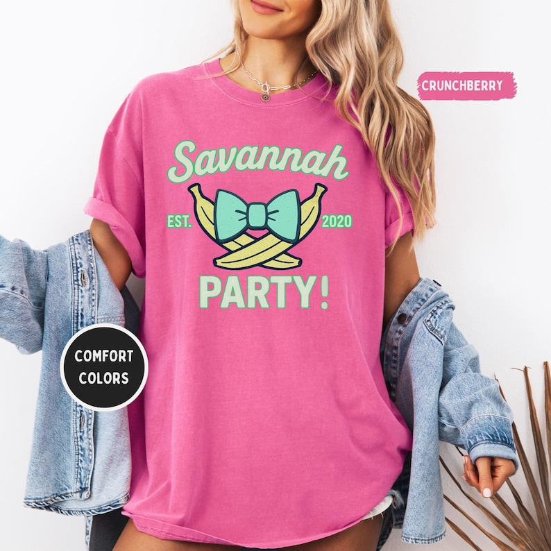 May include: A bright pink t-shirt with the text "Savannah PARTY!" in mint green. The design includes a bow and two bananas. The shirt also has the text "EST. 2020". The shirt is made of Comfort Colors material.