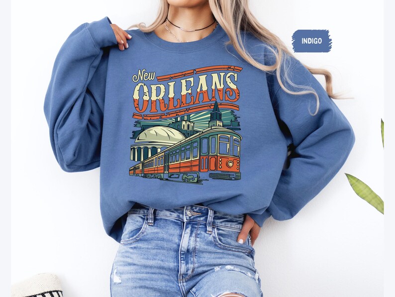 May include: Indigo blue sweatshirt with a graphic print of a streetcar in New Orleans. The text "New Orleans" is printed in white with a red outline.